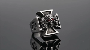 Detail view of punk skull ring with iron cross and red zircon eyes on black surface
