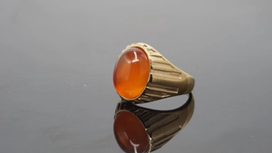 Makroaufnahme eines goldfarbenen Titanrings mit lebhaftem orangerotem Edelstein und Textur
