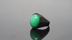 Primer plano de anillo con gema ovalada verde oscuro sobre superficie negra reflectante
