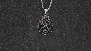 Close-up of Viking Vegvisir compass pendant with Nordic runes on a black textured surface