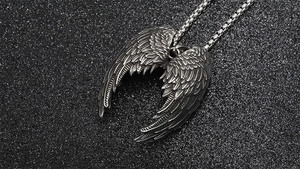 Detailed close-up of retro silver angel wing pendant with textured feathers on dark sand