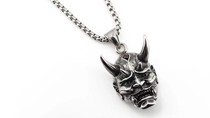 Macro detail of Prajna mask pendant with red garnet inlay and vintage finish on steel