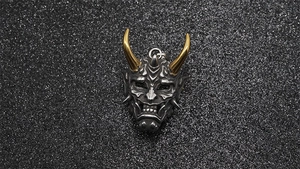 Macro shot of titanium steel Prajna mask pendant with golden horns and dark metal texture