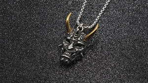 Close-up of titanium steel Oni mask pendant with golden horns and vintage silver finish