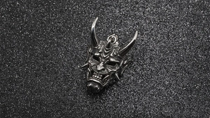 Detailed close-up of a silver-toned Hannya mask pendant with intricate metal engravings