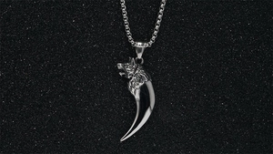 Detailed close-up of a silver wolf head and fang pendant on a stainless steel chain
