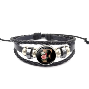 Gedetailleerd zicht op meerlagige leren armband met bloemenletter F en verstelbaar koord
