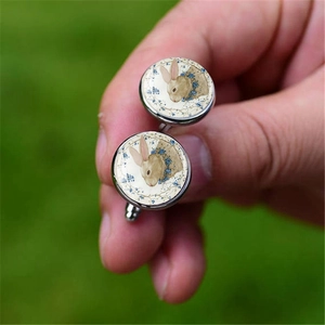 Close-up of silver cufflinks with vintage glass cabochon featuring brown bunny and blue flowers