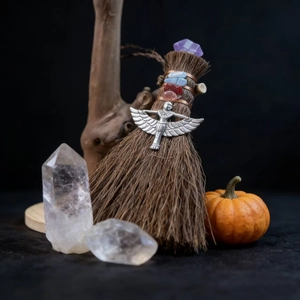 Detail of mini Wicca besom with natural crystals and silver goddess charm on stone surface