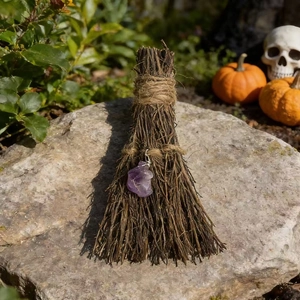 Close-up of handmade witch's broom with purple crystal on stone for Halloween decor
