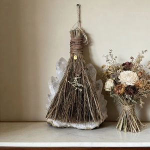 Decorative witch broom with crystal and metal pendant on a white marble background