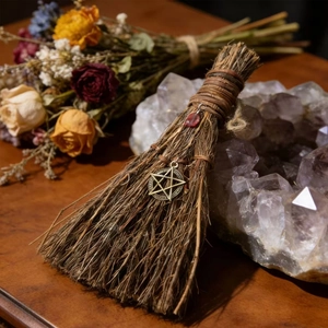 Detail of handcrafted witch broom with pentagram metal charm and red crystal bead decoration
