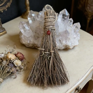 Detail of handmade witch broom with red gemstone and mystical metallic charms