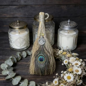 Handmade witch altar besom with peacock feather and gemstone on dark wooden background