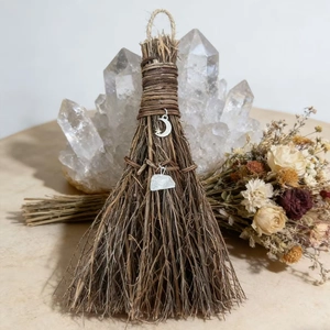 Close-up of decorative witch broom with silver moon charm and white crystal pendant