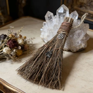 Detail of vintage witch broom with leather wrap, silver pentagram and obsidian crystal