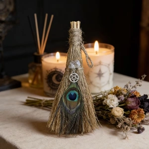 Detail of a handmade witch besom with peacock feather, crystal, and a pentagram charm