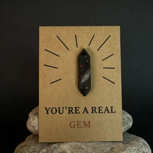 Gepolijste zwarte kristallen steen met rode vlekken op een 'You're a Real Gem' cadeaukaart