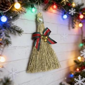 Handmade Christmas witch broom ornament with green gem and bell on a snowy wall