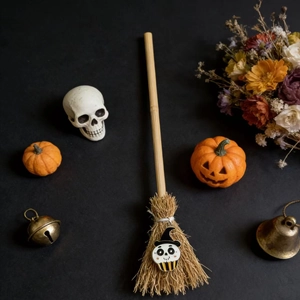 Miniature Halloween witch broom with skull motif and natural straw on black background