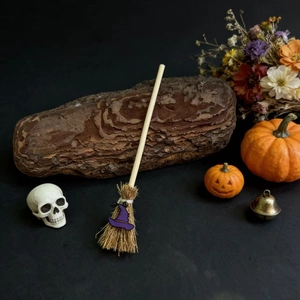 Mini witch broom with purple hat on black background with pumpkin and skull decor