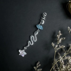 Detail of silver spiral dreadlock jewelry featuring blue raw stone and a star pendant