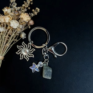 Detail of keychain with sun pendant, iridescent star bead, and green raw stone crystal