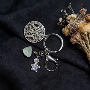 Detail of mystic silver sun keychain with natural green crystal and star on black fabric