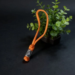 Macro view of orange paracord keychain with Nordic Valknut metal bead on black surface