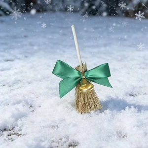 Detail of a Christmas decorative mini broom with green bow, gold bell, and snowy texture