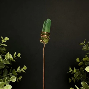 Detail of green crystal prism wrapped in copper wire on a dark background