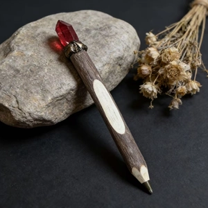 Detailed close-up of a rustic wooden pen with a dark red crystal and vintage metal accents