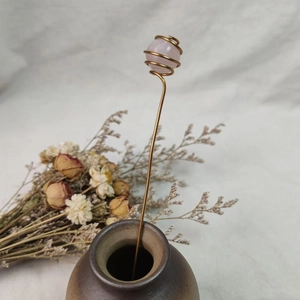 Close-up of handmade rose quartz sphere wrapped in gold wire on a slender metal stem
