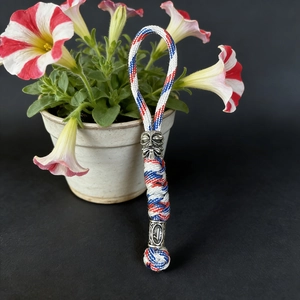 Macro detail of tricolor paracord keychain featuring silver tiki mask and geometric beads