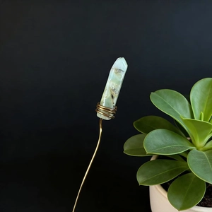 Detailed macro view of handmade green crystal pillar with copper wire wrapping on black background