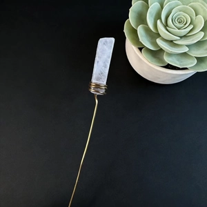 Close-up of natural clear crystal plant stake with copper wire on black background