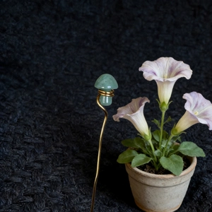 Close-up of green crystal mushroom craft with golden wire wrap in a garden setting
