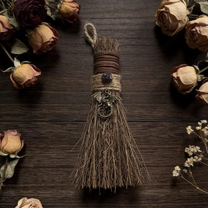 Close-up of handmade witch broom with dragon pendant and purple crystal on dark wood