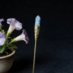 Detailed close-up of a blue crystal hair pin with intricate golden filigree work