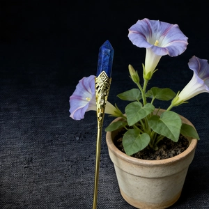 Detailed view of a handmade golden hair pin with a hexagonal deep blue crystal point