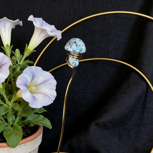 Detail of blue spotted crystal mushroom on golden wire stand with purple flowers