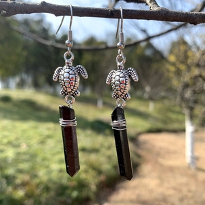Detail of silver turtle earrings with black crystal pendant hanging on a tree branch