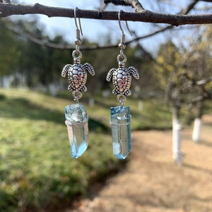 Macro view of turtle-shaped bohemian earrings with light blue crystals on tree branches