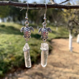 Detail of sea turtle earring with natural white quartz stone hanging on a branch