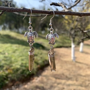Detail of sea turtle crystal earrings with natural brown quartz hanging on a branch
