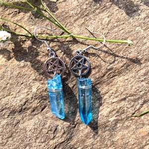 Detail of blue crystal pentagram earrings with wire-wrapped stone on a textured rock
