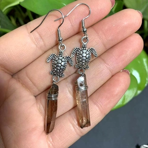 Macro detail of bohemian turtle crystal earrings with dark brown stone on natural green background