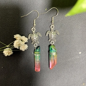 Detail of turtle earrings with colorful crystals and silver wire wrap on black background