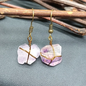 Detailed close-up of wire-wrapped raw amethyst earrings on a rustic wood branch