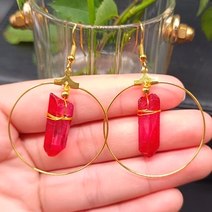 Detail of bohemian gold hoop earrings featuring red crystal pendants held by hand